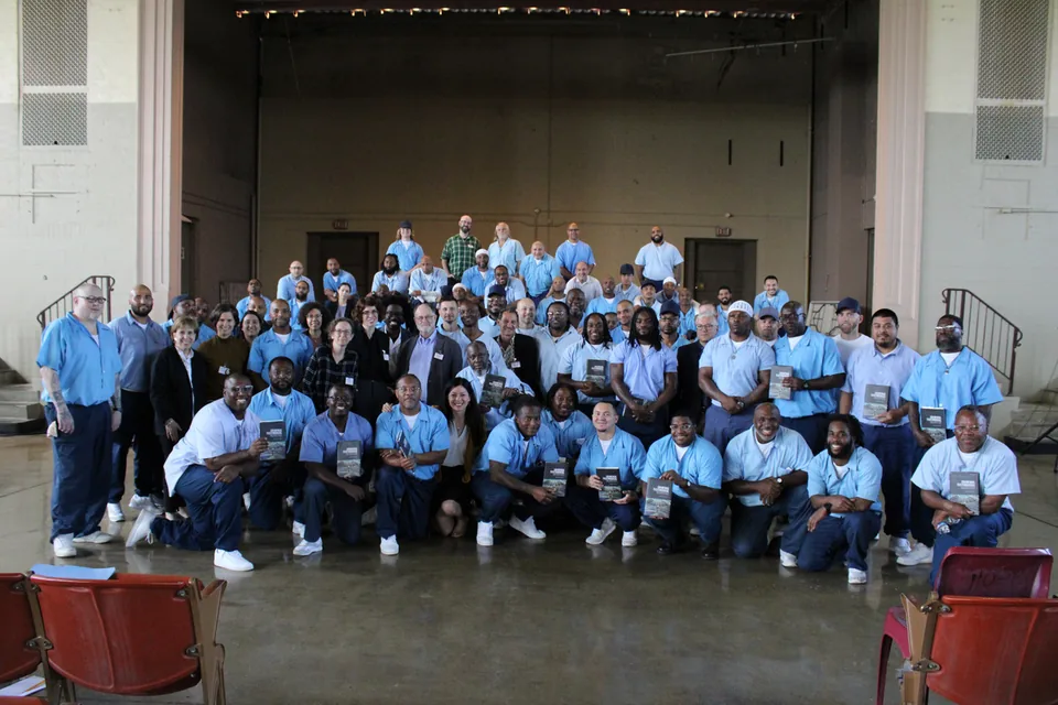 A large group photo of dozens of people, most in light blue uniforms, posed in rows in a hall.