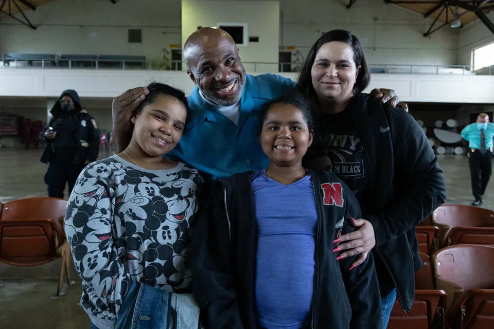 A smiling man in a light blue shirt poses with a woman and two girls in a large room.