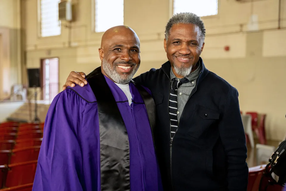 Two smiling men in purple graduation gowns stand together.