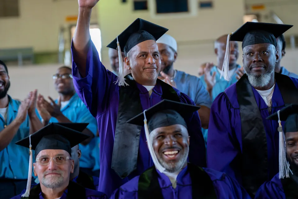 Graduates in purple gowns and mortarboards celebrate; one raises his arm while another smiles in the foreground.