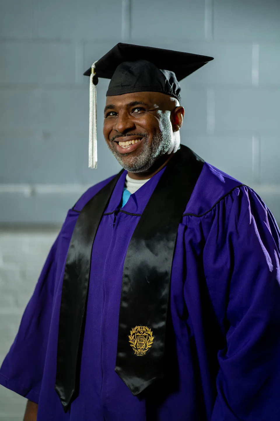 A smiling graduate in a purple gown and mortarboard with a tassel.