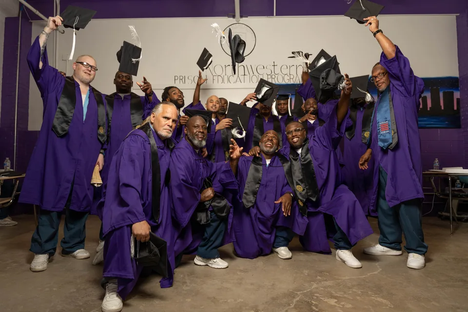 Graduates in purple gowns raise and toss their mortarboards in celebration in front of a Northwestern Prison Education Program mural.