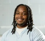 Headshot of a smiling person with shoulder-length locs wearing a white top.
