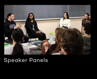 Students sit in a circle of chairs in a classroom listening to a panel of speakers at the front.