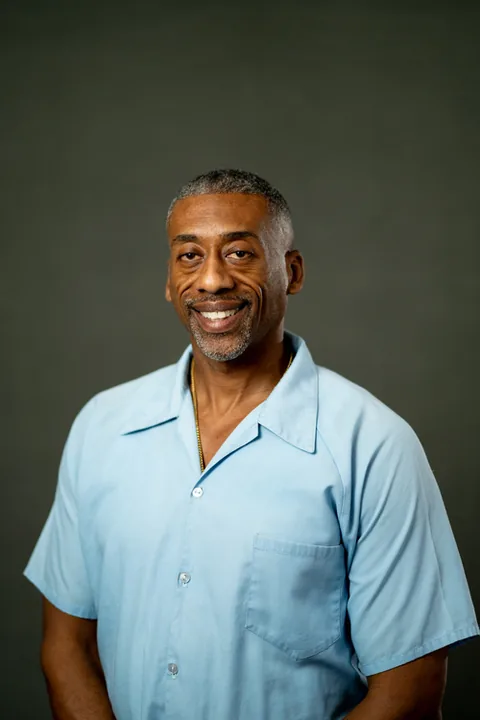 Studio portrait of Anthony Harris, a member of Cohort 5, in a light blue button-up shirt against a dark gray backdrop.