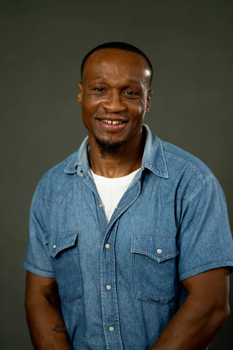 Studio portrait of Darvin Henderson, a member of Cohort 5, in a light blue button-up shirt against a dark gray backdrop.