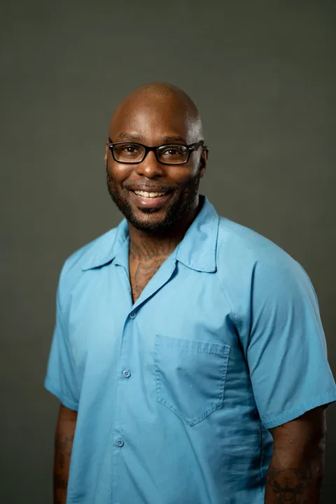 Studio portrait of Falanzo Hixson, a member of Cohort 5, in a light blue button-up shirt against a dark gray backdrop.