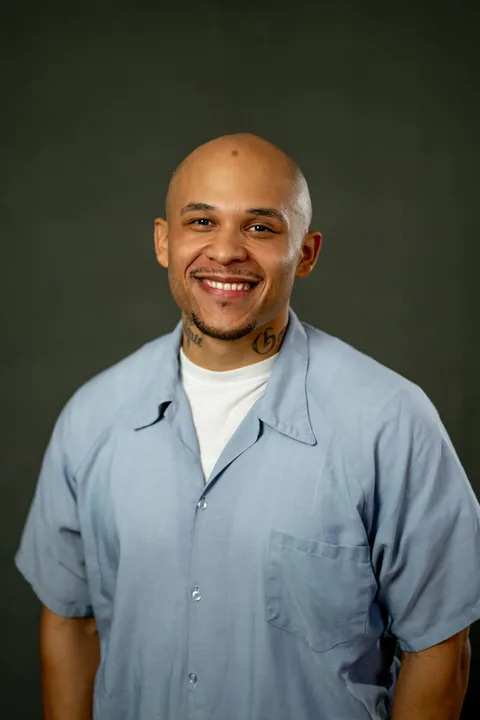 Studio portrait of Giovanni Rios, a member of Cohort 5, in a light blue button-up shirt against a dark gray backdrop.