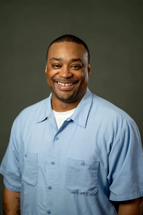 Studio portrait of Stanley Russell, a member of Cohort 5, in a light blue button-up shirt against a dark gray backdrop.