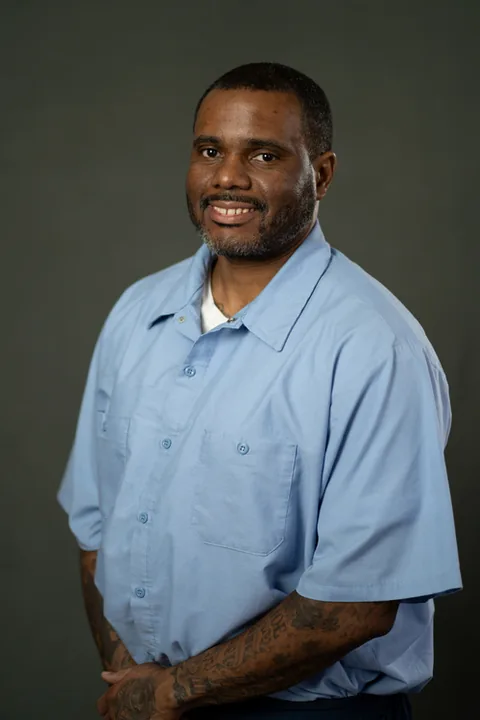 Studio portrait of Jason Samuels, a member of Cohort 5, in a light blue button-up shirt against a dark gray backdrop.