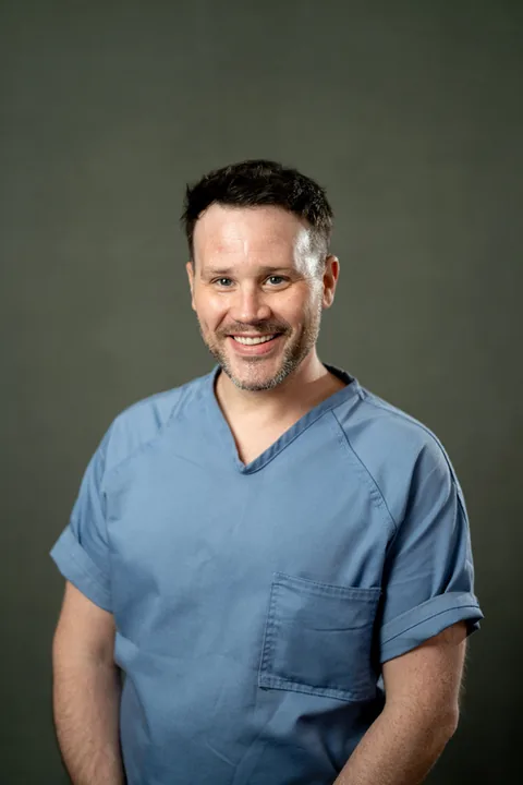 Studio portrait of Scott Sanders, a member of Cohort 5, in a light blue button-up shirt against a dark gray backdrop.