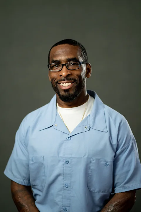Studio portrait of Dahnyah Williams, a member of Cohort 5, in a light blue button-up shirt against a dark gray backdrop.