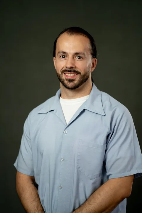 Studio portrait of Orhan Cerimagic, a member of Cohort 5, in a light blue button-up shirt against a dark gray backdrop.