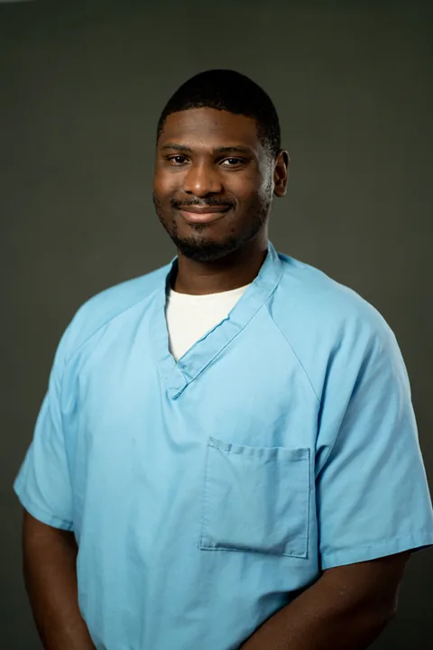 Studio portrait of Justin Foster, a member of Cohort 5, in a light blue button-up shirt against a dark gray backdrop.