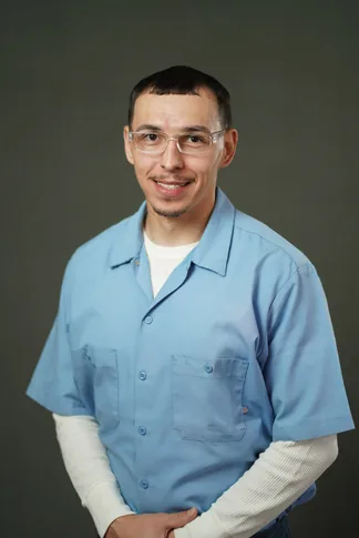 Studio portrait of Nicholas Gacho, a member of Cohort 5, in a light blue button-up shirt against a dark gray backdrop.