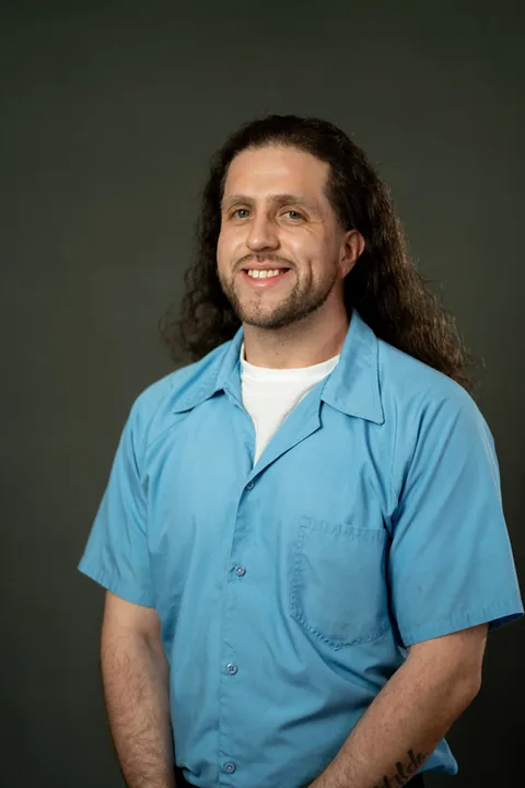 Studio portrait of Juan Garnica, a member of Cohort 5, in a light blue button-up shirt against a dark gray backdrop.