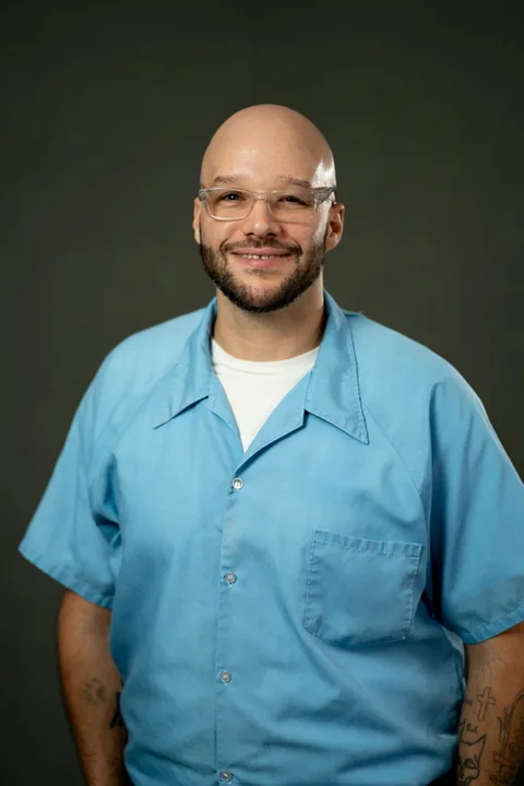Studio portrait of Thomas Gordon, a member of Cohort 5, in a light blue button-up shirt against a dark gray backdrop.