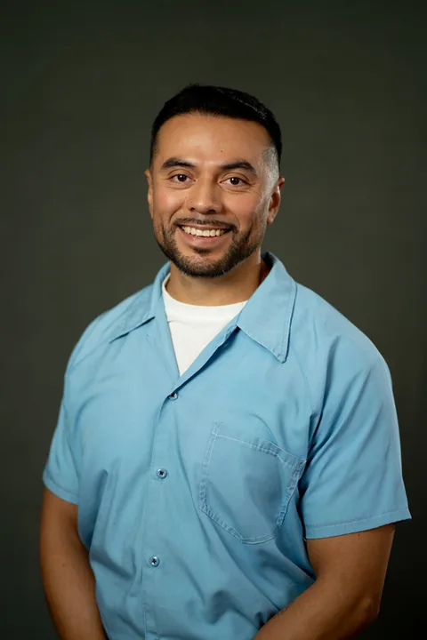 Studio portrait of Oscar Gutierrez, a member of Cohort 5, in a light blue button-up shirt against a dark gray backdrop.