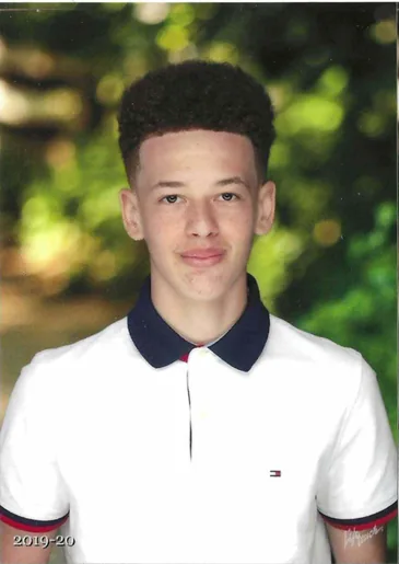 Photo of a teenage boy with curly hair in a white shirt with a dark collar, outdoors.