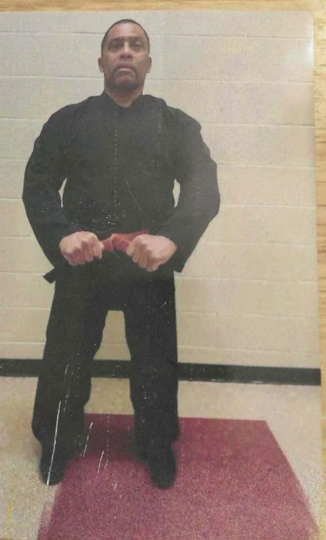 Photo of a man in a dark shirt standing in front of a light wall.